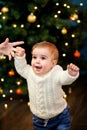 Baby takes first steps holding her mother's hand on the background of the Christmas tree