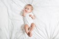 The baby teething Close up portrait of little baby girl in white lying on a white bed. puts her hands in her mouth Royalty Free Stock Photo