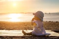 The baby is teething. Everything gnaws, chewing. Infant girl sitting on the tropical sand beach and looking for sunset