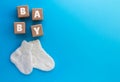 BABY text on wood cubes and pair of cute knitted socks on blue background. Newborn concept. Flat lay, copy space