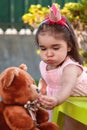 Baby toddler girl, mouth full of candies playing in a tea party feeds best friend Teddy Bear with candy Royalty Free Stock Photo