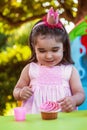 Baby toddler girl in outdoor party at garden, happy and smiling at cupcake with sweet tooth expression