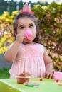 Baby toddler girl playing in outdoor tea party drinking from cup with lollipop, muffin and gummies on table Royalty Free Stock Photo