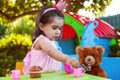 Baby toddler girl playing in outdoor tea party serving her best friend Teddy Bear with candy gummy Royalty Free Stock Photo