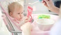 Baby with toy sitting in chair and eating puree. Mother feeding baby with spoon Royalty Free Stock Photo