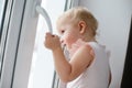 Baby is trying to open the window in the apartment. No lock on the window. Dangerous home for a baby. Fall safety for children. Royalty Free Stock Photo