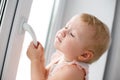 Baby is trying to open the window in the apartment. No lock on the window. Dangerous home for a baby. Fall safety for children. Royalty Free Stock Photo