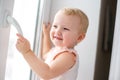 Baby is trying to open the window in the apartment. No lock on the window. Dangerous home for a baby. Fall safety for children. Royalty Free Stock Photo