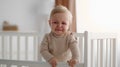 Baby unhappiness. Portrait of adorable unhappy crying baby standing in crib, suffering from colics or teething