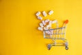 Baby vitamins in the form of bears fell out of the toy carts for products. On a bright yellow background. Pharmaceutical concept Royalty Free Stock Photo