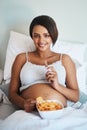 The baby wants what it wants. Portrait of an attractive young pregnant woman eating potato chips and chocolate in bed. Royalty Free Stock Photo