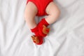 Baby wearing festive Christmas socks on white bedsheet, top view