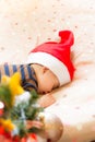 Baby wearing Santa Claus hat sleeping by Christmas tree