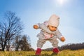 Baby wearing warm beanie hat, sweatshirt and red boots outdoors in rural area discovering nature in spring, sunny day Royalty Free Stock Photo