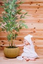 The baby wrapped in a white towel sitting on wooden background near a bamboo tree in pot