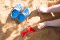 baby& x27;s legs in the beach sand, blue flip flops and a toy shovel, play in the sandbox