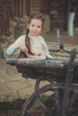 Baby young girl with blue eyes with brunnette plait hair wearing white dress shirt and posing on wooden old style retro wagon cart