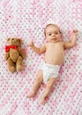 Baby girl in diaper lying with teddy on blanket