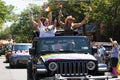 Women standing up in a jeep waving gay pride flags during parade