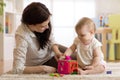 Babysitter looking after baby. Child plays with sorter toy sitting on the carpet at home