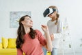 Babysitter looking at cheerful kid in virtual reality headset