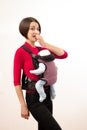 Babywearing confused young mother with baby in not ergonomic carrier. Isolated on white