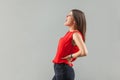 Back ache or pain on kidney. Profile side view portrait of screaming sick brunette young woman in red shirt standing and holding