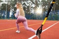 Back angle view of sporty fitness woman in pink clothes training with trx fitness straps at the red coated court Royalty Free Stock Photo