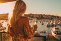 Back beautiful slim chic girl with long blond hair in golden dress with champagne glass in hand background of the bay of yachts in Royalty Free Stock Photo