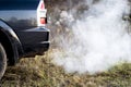 The back of the black car with the emission of smoke from the exhaust pipe on the background of nature