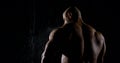 Back brutal muscular male bodybuilder close-up on a black background, he is in the rain, water flows down it Royalty Free Stock Photo