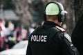 Back of a Calgary Police officer wearing ear protection and a neon green baseball cap at a protest