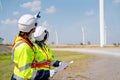 Back of Caucasian engineer man and woman discuss together with woman hold drawing paper and stay in front of row of windmill or Royalty Free Stock Photo