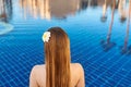 Back of the caucasian woman with log hair and flower in it sitting on the edge of the swimming pool. Royalty Free Stock Photo