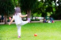 Back of child is playing kicking small orange ball on green lawn. Asian girl wearing white shirts and playing sports. Royalty Free Stock Photo