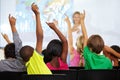 Back of children, teacher and raise hands for questions, education or learning with geography quiz in classroom. Youth Royalty Free Stock Photo