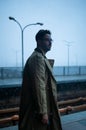 Back of cinematic man in winter coat walking outside in urban city on bridge on a moody, foggy, winters night. Royalty Free Stock Photo