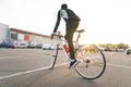 Back of a cyclist rides on a white highway bike on car parking, sunset and modern architecture on the background