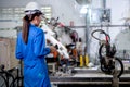 Back of factory worker woman hold controller to control metal welding robotic machine and work in workplace area. Industrial and Royalty Free Stock Photo