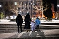 Back of family walk through the night city in the winter. Mother and three children in evening Royalty Free Stock Photo