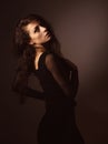 Back female view. Beautiful elegant sensual woman with brown long hair and black dress looking on dark shadow background. Royalty Free Stock Photo