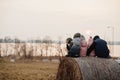 Back of four kids sitting on haycock at field against lake sunset Royalty Free Stock Photo