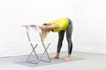 Back and hamstrings stretching, yoga indoor with a props. Caucasian woman does deep bend holding on to the chair with