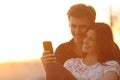 Back light of a couple sharing a smart phone Royalty Free Stock Photo