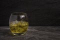 A back lit oval glass of golden Whiskey with ice on a stone base against a rock background Royalty Free Stock Photo