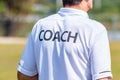 Back of male sport coach wearing COACH shirt at an outdoor sport field