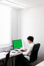 Back of the man wearing white shirt and sit on black office chair, working with his personal computer with green screen display. Royalty Free Stock Photo