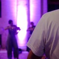 Back of a man in a white shirt. In the background a girl plays the violin in the night lights Royalty Free Stock Photo