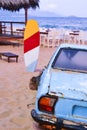 The back of an old blue car parked on a tropical beach of the sea coast. A colored surfboard stands upright in the sand. Rest in Royalty Free Stock Photo
