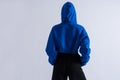 Back photo of an anonymous girl in blue hoodie with hood on and pants. Hands in pockets.